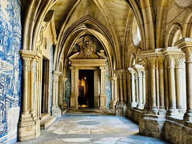 Un pasillo de piedra en el claustro con arcos góticos y los tradicionales azulejos azules.
