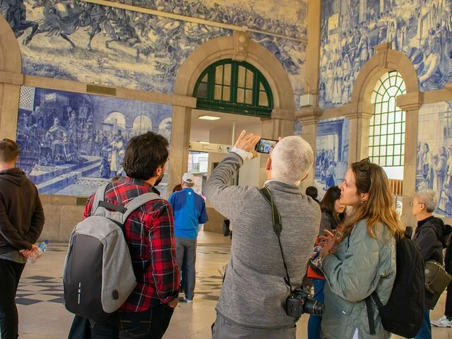 Gente tomando fotos y admirando los murales de azulejos azules dentro de una estación.