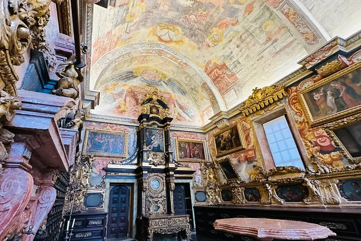 Una sala interior ornamentada con techos pintados, obras de arte con marcos dorados y decoración religiosa.
