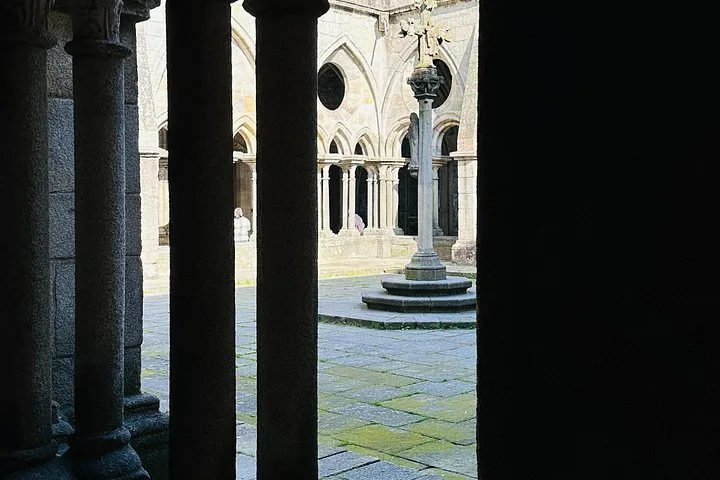 A view through stone pillars into a gothic cloister courtyard with a cross.